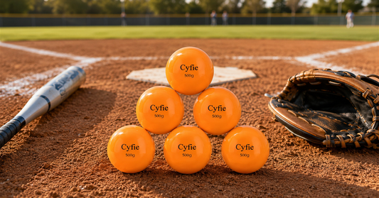 CYFIE weighted softball training balls beside a bat and pitcher's glove on a softball practice field