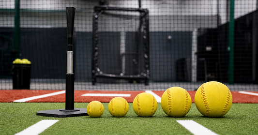 Several weighted softballs arranged from light to heavy beside a practice tee