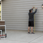 Adult measuring wall height and court clearance before mounting a basketball hoop