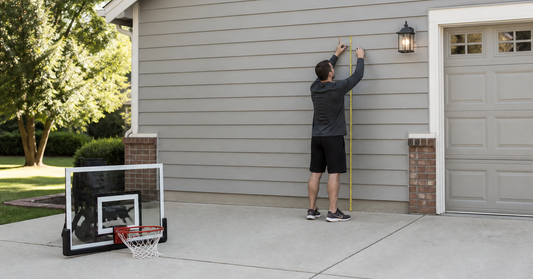 Adult measuring wall height and court clearance before mounting a basketball hoop