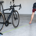 Cyclist measuring a bicycle wheel rollout beside a wireless bike computer and sensor
