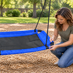 Adult inspecting the blue edge of an empty CYFIE rectangular platform swing in a backyard