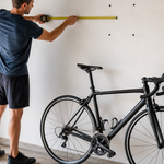 Person measuring wall and bicycle clearances before installing a swivel wall-mounted bike rack in a garage