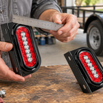 Adult checking the bracket on a red oval CYFIE trailer light at a garage workbench