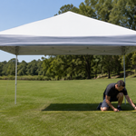 Adult measuring an existing canopy frame beside a folded green sidewall on a calm day
