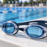 Blue-lensed swim goggles with an adjustable strap beside a swimming pool